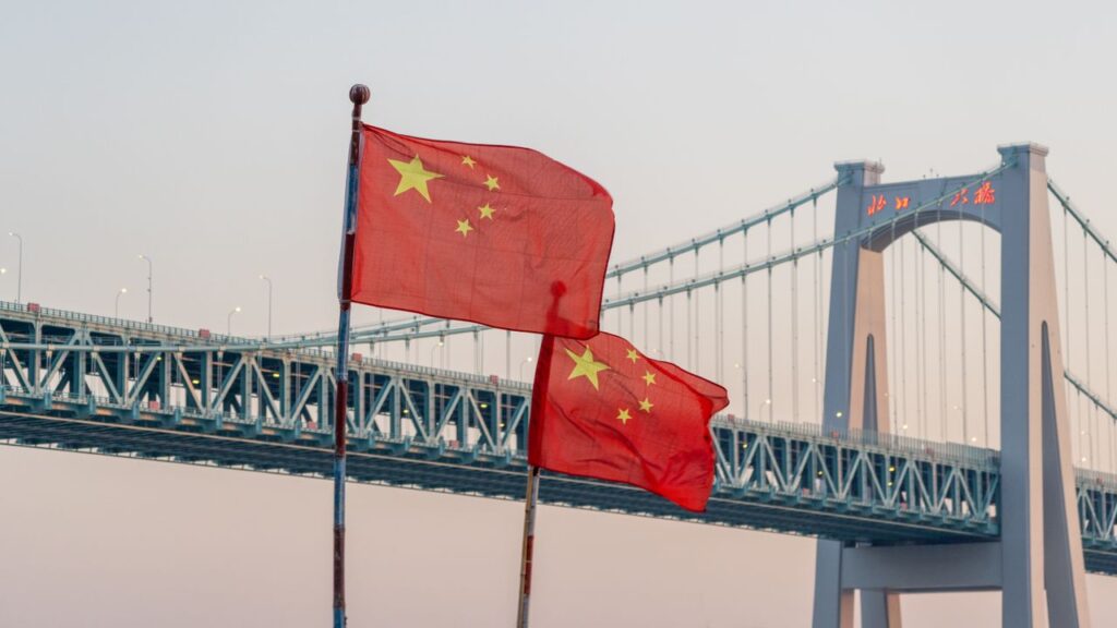 Chinese flags waving in front of a bridge at sunset, showcasing national pride and architecture.